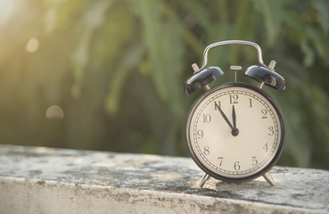 black alarm clock on table at morning in garden background.