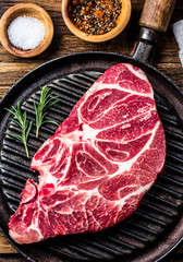 Raw beef marbled meat steak on vintage cast iron grill pan, spices and carving meat set on wooden rustic background. Top view