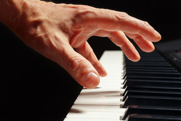 Hand of pianist play the keys of the electronic piano on a black background close up