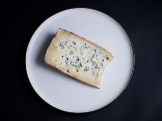 Slice of french blue cheese made from cows milk on white rustic plate isolated on black background