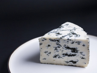 Slice of french blue cheese made from goats milk on rustic white plate, isolated on black background