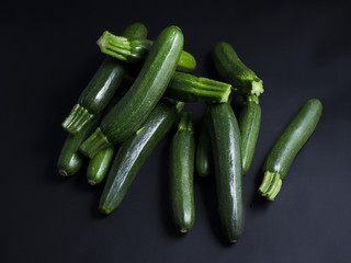 Green baby zucchinis in a pile isolated on black background