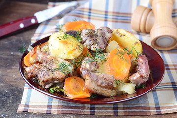 Oven cooked pork with potato, carrots and onion in olive oil and spices in a brown ceramic plate on a wooden background. Home cooking
