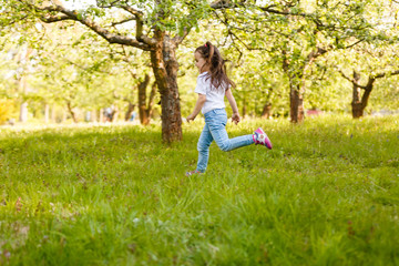 little girl blows off fluff from a bouquet of dandelions, standing in the middle of an apple orchard