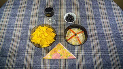 Bowl of tuna salad, tortilla chips, olives and glass of red wine.