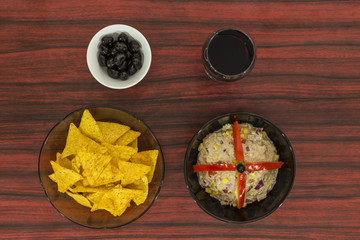 Bowl of tuna salad, tortilla chips, olives and glass of red wine.