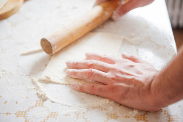 On the table the flour of the hand of the cook roll out the dough, the ingredients.