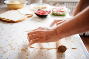 On the table the flour of the hand of the cook roll out the dough, the ingredients.