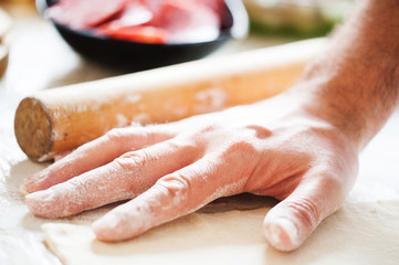 On the table the flour of the hand of the cook roll out the dough, the ingredients.