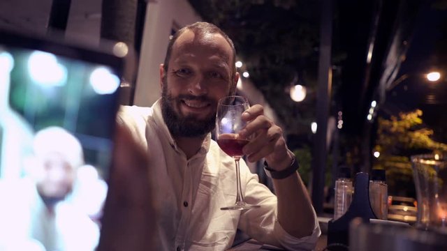 Young man taking selfie photo with cellphone and drinking cocktail in cafe at night 

