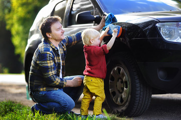 Middle age father with his toddler son washing car together outdoors