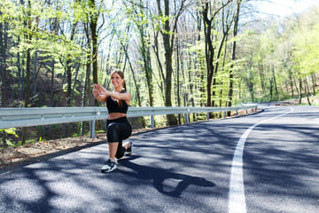 Young sports woman stretching his muscles before running in the woods on the  road.
