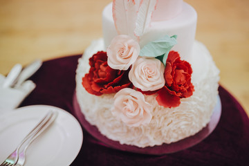 Three-tiered wedding cake is decorated with flowers and stands on the table next to a plate and cutlery