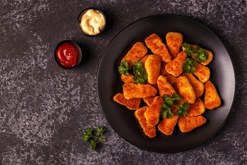 Chicken nuggets with sauces on dark background.
