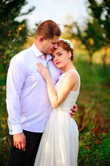 The bride and groom are kissing in the apple orchard, standing under the branches of an apple-tree