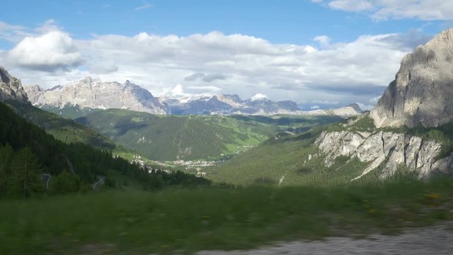 Driving side window POV coming down from Passo Gardena (Gardena Pass) towards Alta Badia, Northern Italy. Prominent Dolomites peaks include La Varella and Cunturines of the Fanes Group.