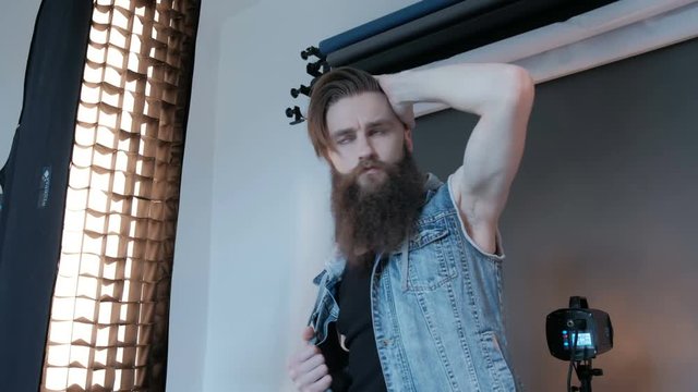 Photographer taking pictures for man model in studio with blue background. Guy model with a long beard. Shooting fashion catalog
