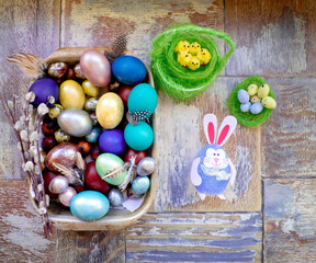 On the old wooden shabby table a dish of metal with painted in different colors Easter eggs with feathers willow and chickens with rabbit