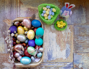 On the old wooden shabby table a dish with painted in different colors Easter eggs with feathers willow and chickens with rabbit