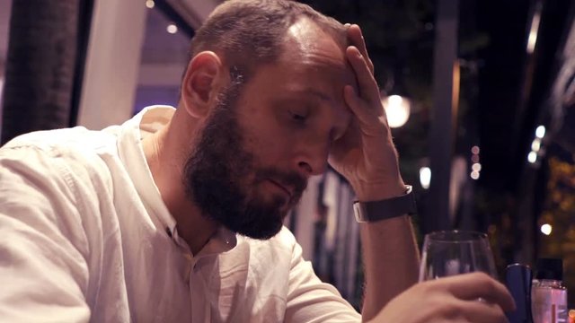 Sad, unhappy man drinking wine sitting in cafe during evening 

