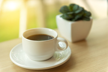 Coffee in white cup on wood table with morning sunlight