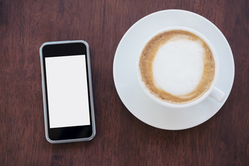 Mockup image of black mobile phone with blank white screen and hot latte coffee on vintage wooden table in cafe
