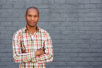 cool young african man standing by gray wall with arms crossed