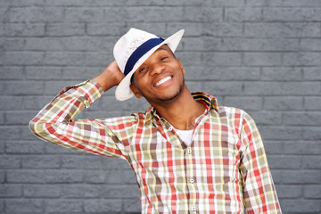 happy african american guy with hat smiling in front of grey wall