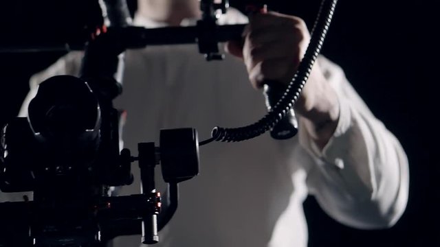 Smooth movement of the camera in the protective cage installed on the stabilizer in the hands of the operator focusing on the screen recorder.