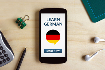 Learn german concept on smart phone screen on wooden desk. All screen content is designed by me. Flat lay © maicasaa