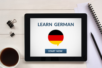 Learn german concept on tablet screen with office objects on white wooden table. All screen content...