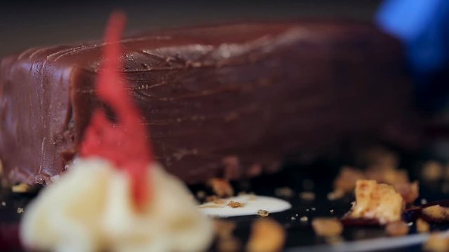 panoramic refocusing closeup shot of put a piece of chocolate on a plate. Chocolate dessert in a restaurant. Decorated with honey crumbs, creamy stars and red sweet decorative elements.
