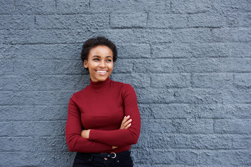 attractive smiling african woman leaning against gray wall