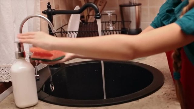 Child hands moisten and foam a sponge - preparing to wash dishes at the kitchen sink