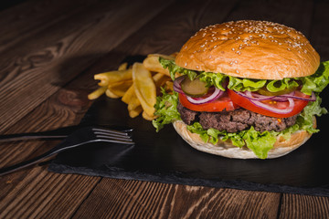 Fresh burger in bun with sesame with lettuce, tomato, beef and onion on wooden table.