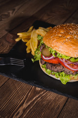 Fresh burger in bun with sesame with lettuce, tomato, beef and onion on wooden table.