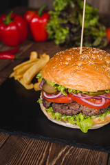 Fresh burger in bun with sesame with lettuce, tomato, beef and onion on wooden table.