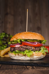 Fresh burger in bun with sesame with lettuce, tomato, beef and onion on wooden table.