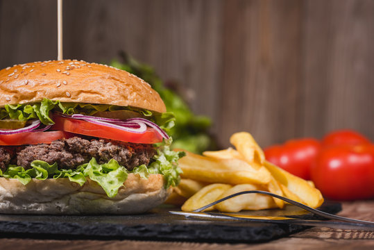 Fresh burger in bun with sesame with lettuce, tomato, beef and onion on wooden table.