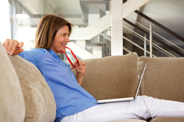 Obraz premium happy older woman sitting on sofa looking laptop