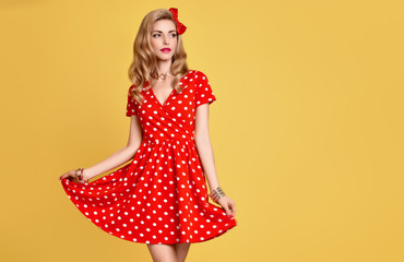 Fashion Beauty. PinUp Sensual Blond Girl Smiling in Red Polka Dots Summer Dress. Woman in fashion pose. Trendy Stylish Curly hairstyle, fashion Makeup, red Bow. Glamour Playful Sexy pinup Model Lady