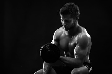 Monochrome studio shot of a young handsome male bodybuilder lifting weights working out with...
