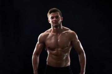 Fototapeta na wymiar Handsome young shirtless athletic man smiling to the camera posing confidently on black background showing off his sexy strong body six-pack abs muscles fitness happiness lifestyle sports motivation.