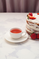 strawberry cake with cup of tea, front view, vertical. Homemade cake with strawberry cream and a cup of tea