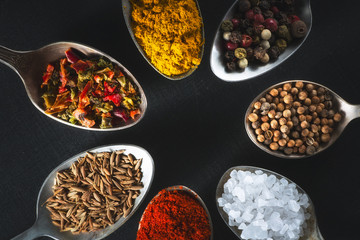 spoons with salt and spices on black chalkboard