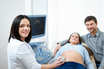Beautiful female doctor smiling to the camera while examining her pregnant patient copyspace couples family healthcare medicine professionalism sonogram pregnancy ultrasound scanning hospital.