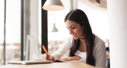 Young woman writing in her notebook and drinking morning coffee