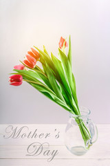 happy mother's day text sign on pink tulips on white rustic wooden background. greeting card concept. sensual tender women image. spring flowers flat lay