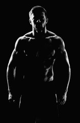 Vertical black and white silhouette of a shirtless athletic man with muscular strong body posing confidently on black background masculine brutal sportsman bodybuilder fitness athleticism concept.
