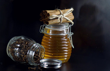 Fototapeta na wymiar a jar of honey and cinnamon sticks on black background, horizontal